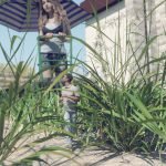 A young giantess woman is mowing her backyard while a miniaturized person is making his way through the same yard